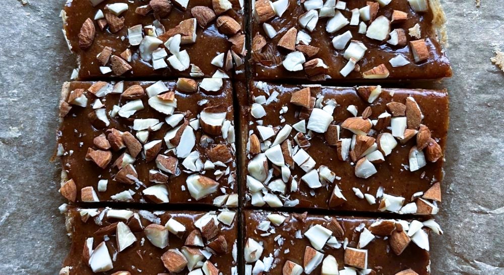 Proteinbarene etter at laget med mandelsmørmasse er lagt på og mandler drysset over. Proteinbarene etter at laget med mandelsmørmasse er lagt på og mandler drysset over.