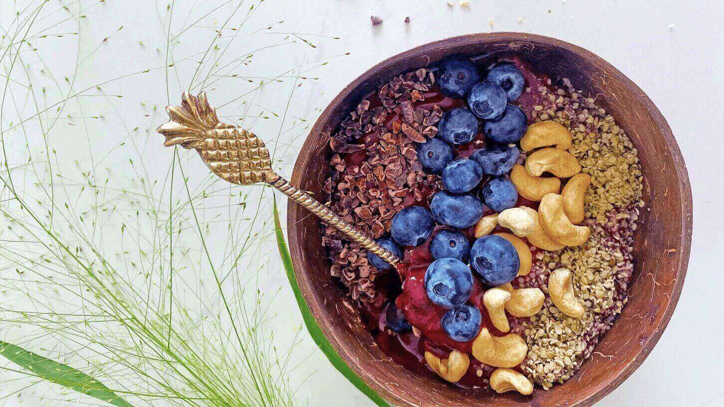 Acai bowl er sunt og godt En acai bowl med blåbær, nøtter og skåret sjokolade i en bolle, med en skje i gull med ananas i enden.