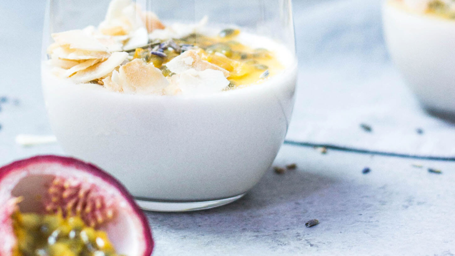 En hvit bolle med yoghurt, pasjonsfrukt og kokosflak på et hvitt steinbord