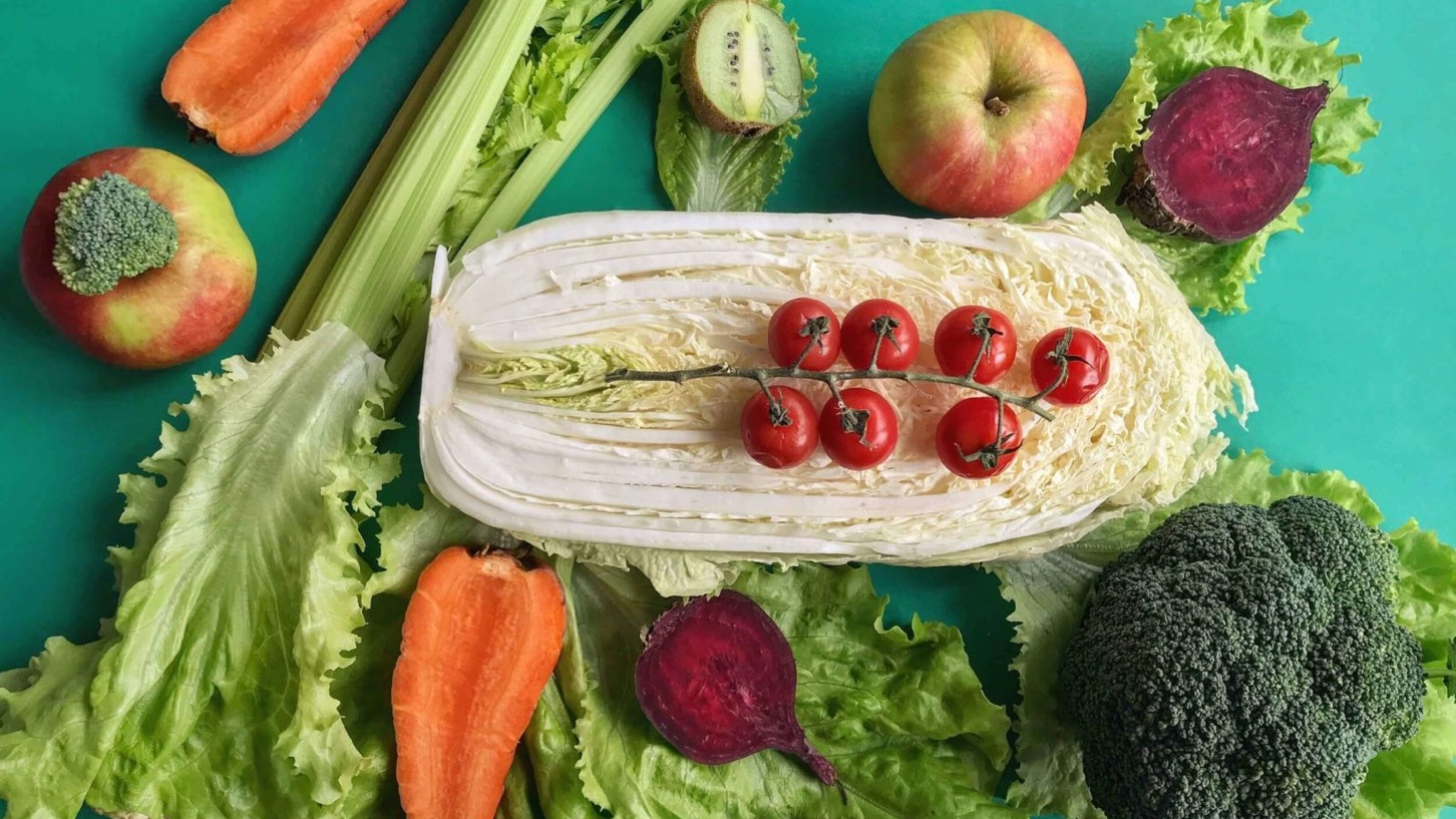 Et grønt bord med grønnsaker som salat, tomat, rødbeter, eple, brokkoli og andre sunne produkter.