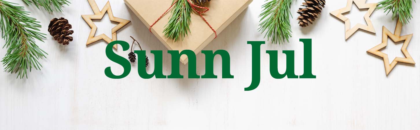 Sunkost ønsker deg en sunn jul med grønn tekst ved hvit trebakgrunn der det ligger juledetaljer som pakker, pyntestjerner og kongler.