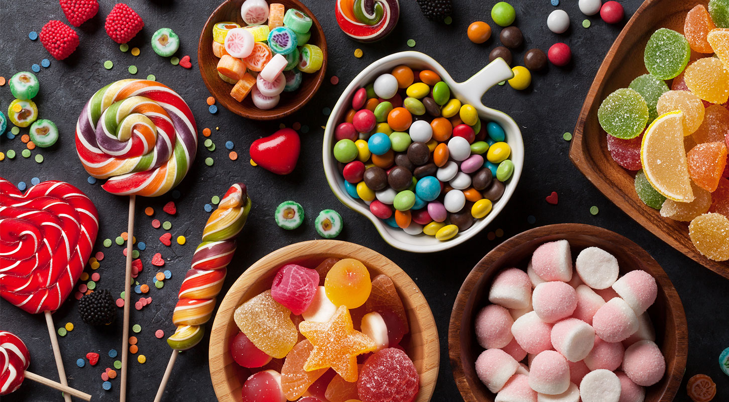 Masse forskjellige godteri fordelt i skåler på et bord med kjærlighet på pinner og fargerik pynt.